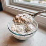 A spoonful of creamy, thick chia seed pudding being lifted from a clear glass bowl.