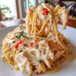 Close-up of creamy chicken spaghetti with melted cheese being lifted by a fork, showing stringy cheese.
