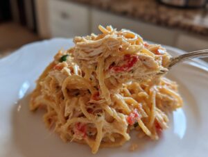 Close-up of creamy chicken spaghetti with shredded chicken and red peppers being lifted high on a fork.