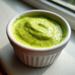 Close-up of vibrant green, creamy cilantro lime sauce swirled in a small white ramekin.