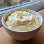 A close-up of a small white bowl filled with thick, creamy, homemade garlic aioli recipe.