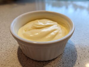A close-up of creamy, pale yellow homemade garlic aioli recipe served in a small white ramekin.