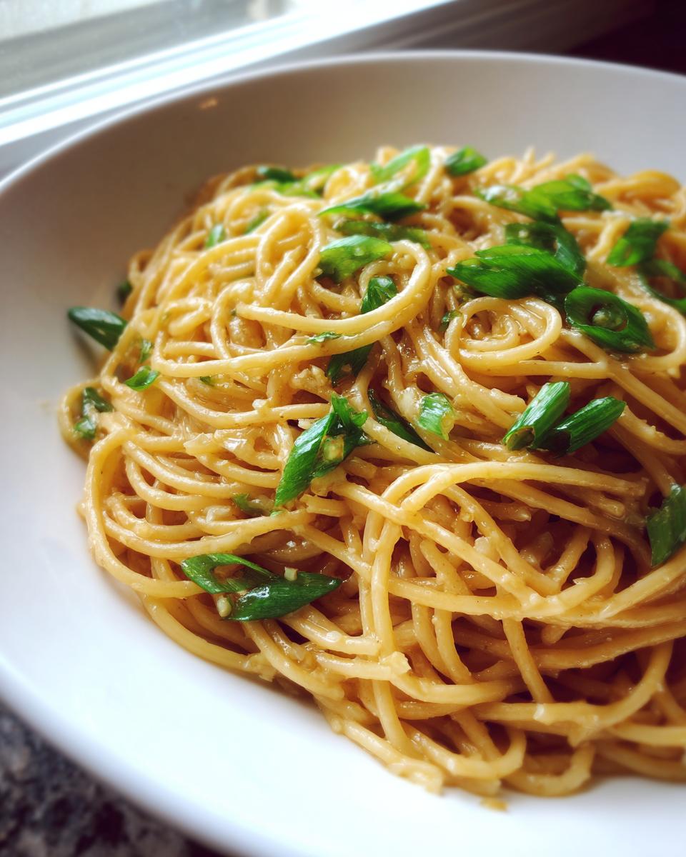 A close-up view of creamy, saucy garlic noodles topped generously with sliced green onions in a white bowl.