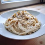 A plate of fettuccine pasta generously coated in creamy cottage cheese alfredo sauce and topped with black pepper.