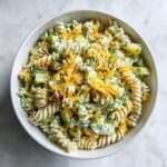 Overhead view of a bowl of creamy pickle pasta salad mixed with dill and topped with shredded cheddar cheese.