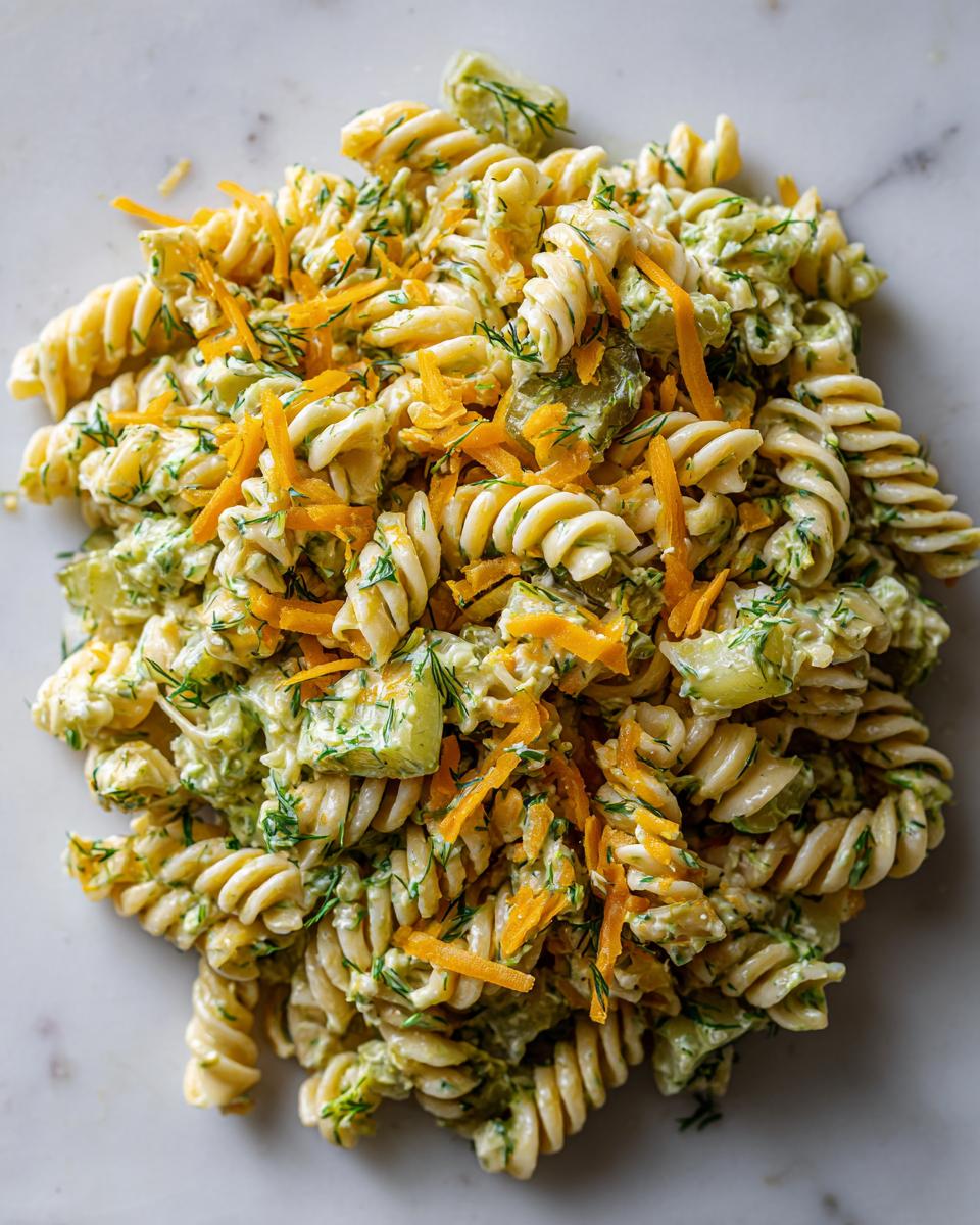 Overhead view of creamy pickle pasta salad made with rotini pasta, dill, and topped with shredded cheddar cheese.