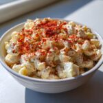 Close-up of creamy deviled egg pasta salad topped generously with bright red paprika.