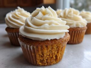 Close-up of a fluffy pumpkin spice cupcake topped with a swirl of cream cheese frosting.