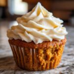 Close-up of a fluffy pumpkin spice cupcake topped with a swirl of cream cheese frosting.