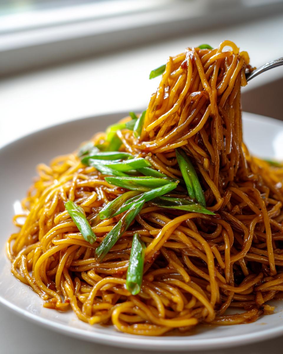 A fork lifts a tangle of saucy, brown garlic noodles topped with bright green scallions from a white plate.