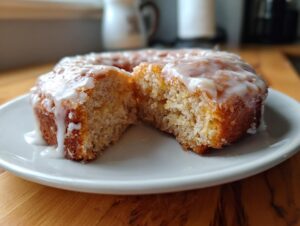 A close-up view of a cake donuts broken in half, showing the moist interior and thick white glaze dripping down.