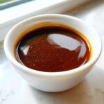 Close-up of rich, dark brown teriyaki sauce glistening in a small white dipping bowl.