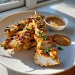Close-up of grilled chicken satay skewers, garnished with parsley, served with peanut dipping sauce.