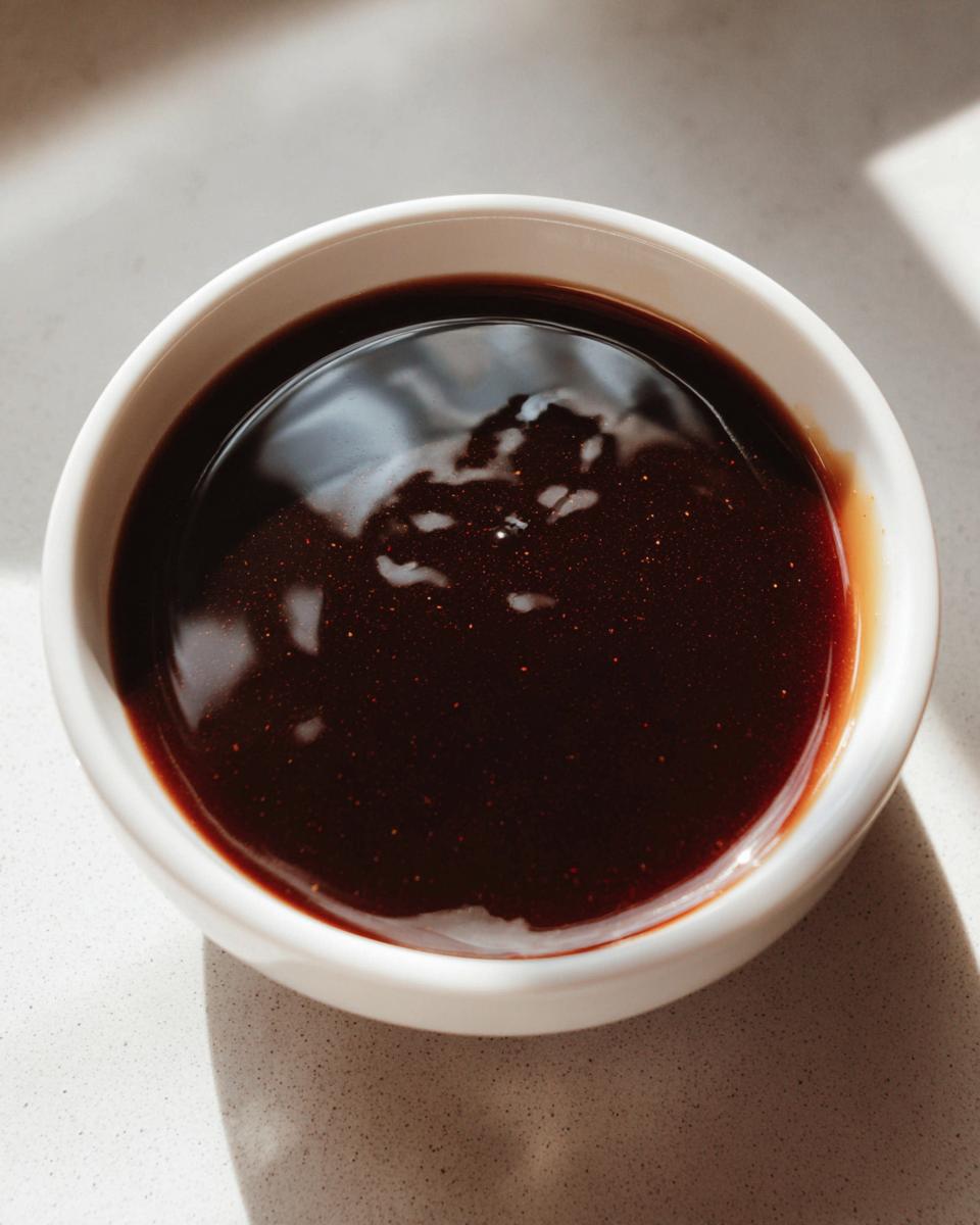 Close-up of thick, dark, glossy teriyaki sauce in a small white dipping bowl.