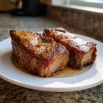 Two thick, perfectly seared and seasoned pork steak pieces resting in their juices on a white plate.