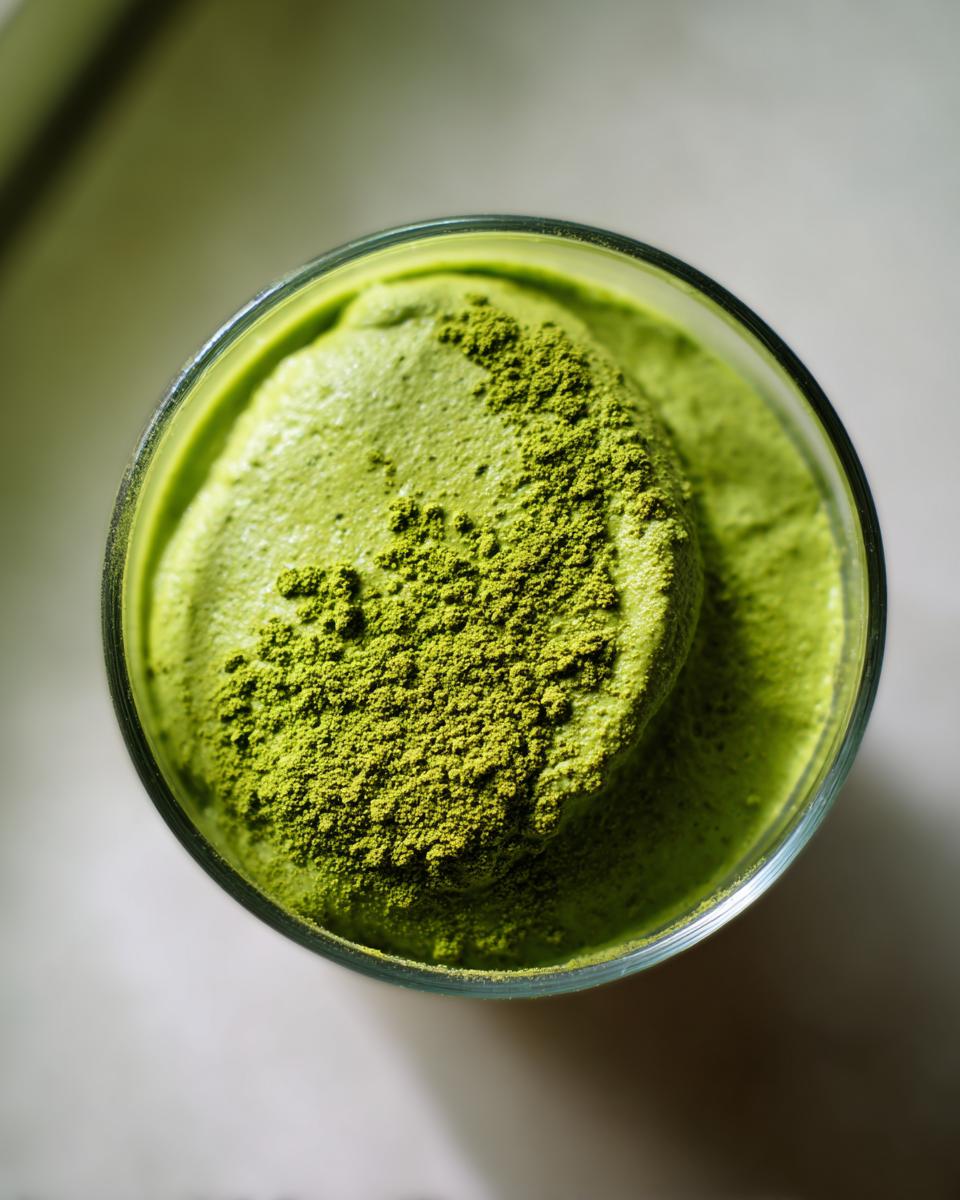 Overhead view of vibrant green matcha chia pudding topped with extra matcha powder in a glass.