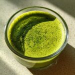 Overhead close-up of vibrant green matcha chia pudding with a foamy top in a small glass jar.