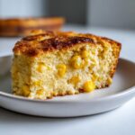 Close-up of a moist slice of jiffy corn casserole showing whole corn kernels baked inside.