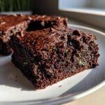 A close-up of a rich, dark chocolate zucchini brownies square showing green flecks of zucchini and chocolate chips.
