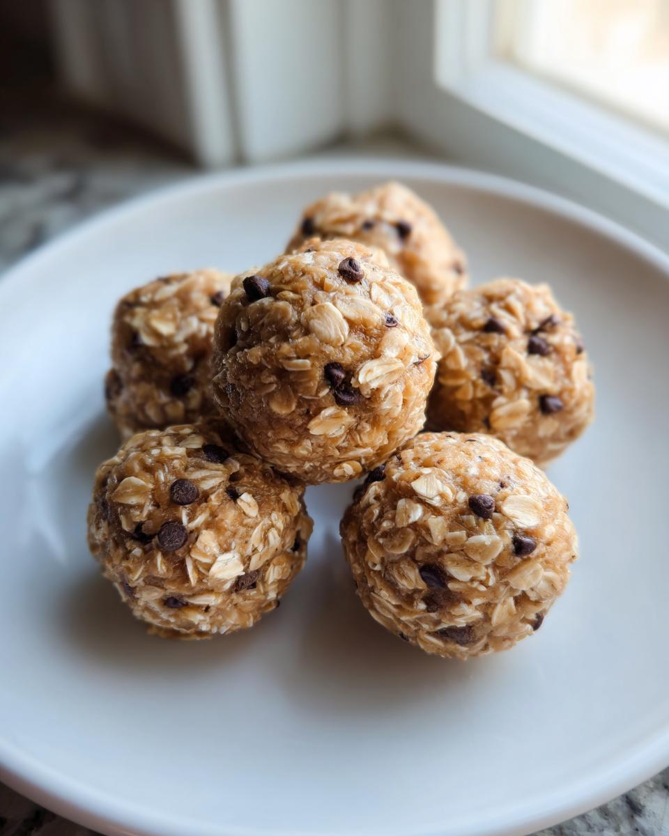 A stack of six homemade, no-bake protein balls studded with oats and mini chocolate chips on a white plate.