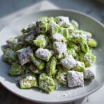 Close-up of bright green pistachio puppy chow heavily dusted with powdered sugar on a white plate.