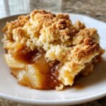 Close-up of a serving of warm apple cobbler with a crumbly topping and gooey cinnamon apples.