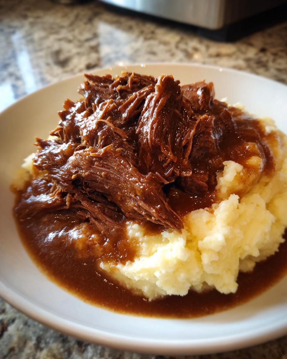 Close-up of shredded beef smothered in rich brown gravy served over mashed potatoes, perfect for a slow cooker beef manhattan recipe.