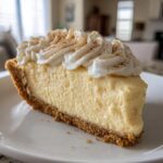 A thick slice of creamy, pale yellow eggnog pie with a graham cracker crust, topped with whipped cream and cinnamon.