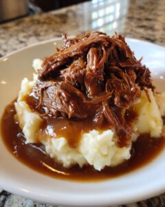 A close-up of shredded beef in rich brown gravy served over mashed potatoes, perfect for a slow cooker beef manhattan recipe.