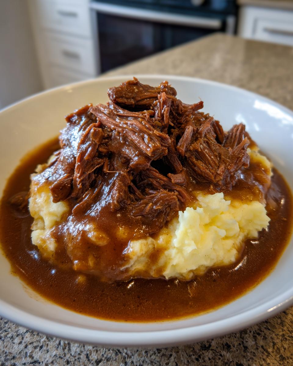 A bowl of creamy mashed potatoes topped with shredded beef and rich brown gravy from a slow cooker beef manhattan recipe.