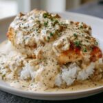 A perfectly cooked piece of smothered chicken and rice topped with a creamy, savory sauce and fresh herbs.