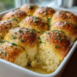 Close-up of soft, golden brown buttery rolls soaking in garlic butter and topped with fresh parsley.