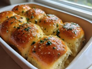 Close-up of freshly baked, golden brown, soft buttery rolls topped with melted butter and chopped parsley.