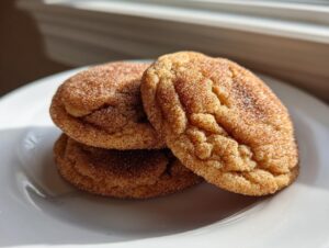 Close-up of three soft, chewy cinnamon cookies generously coated in cinnamon sugar, sitting on a white plate.