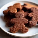 A close-up of several soft gingerbread cookies shaped like people piled on a white plate.