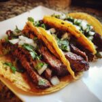 Close-up of three authentic steak tacos filled with sliced grilled steak, diced white onion, and fresh cilantro.