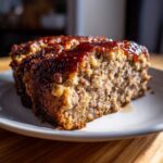 Close-up of a thick slice of stove top stuffing meatloaf topped with a shiny brown glaze.