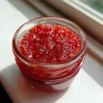 Close-up of bright red, glistening strawberry freezer jam texture inside a clear glass jar.