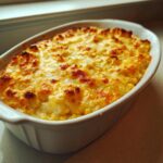 A freshly baked, cheesy, golden-brown corn dip in a white oval baking dish.
