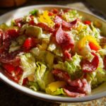 A vibrant bowl of grinder salad featuring crisp lettuce, salami slices, red and yellow bell peppers, coated in a creamy dressing.