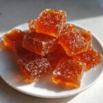 A pile of sparkling, amber-colored Probiotic Gummy Jello bites resting on a small white plate.
