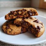 Close-up of soft banana bread chocolate chip cookies, one broken open showing gooey melted chocolate chips inside.