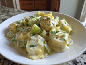 Close-up of tender braised leeks and pasta in a creamy white sauce, garnished with pepper and herbs.