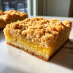 A close-up of a single square Cake Picnic Bar showing a thick, golden crumb topping over a layer of yellow filling and cake base.