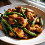 Close-up of tender pieces of chicken and bright green beans coated in a rich, dark sauce in a white bowl, perfect for chicken and green bean stir fry.