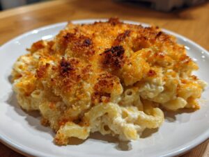 A close-up of a serving of creamy chicken pasta casserole with a crispy, golden-brown cheese and breadcrumb topping.