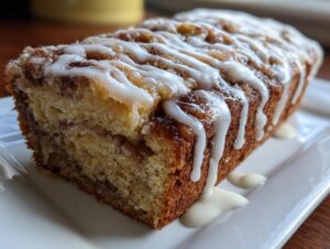 A close-up of a freshly baked cinnamon roll banana bread loaf drizzled generously with white icing.