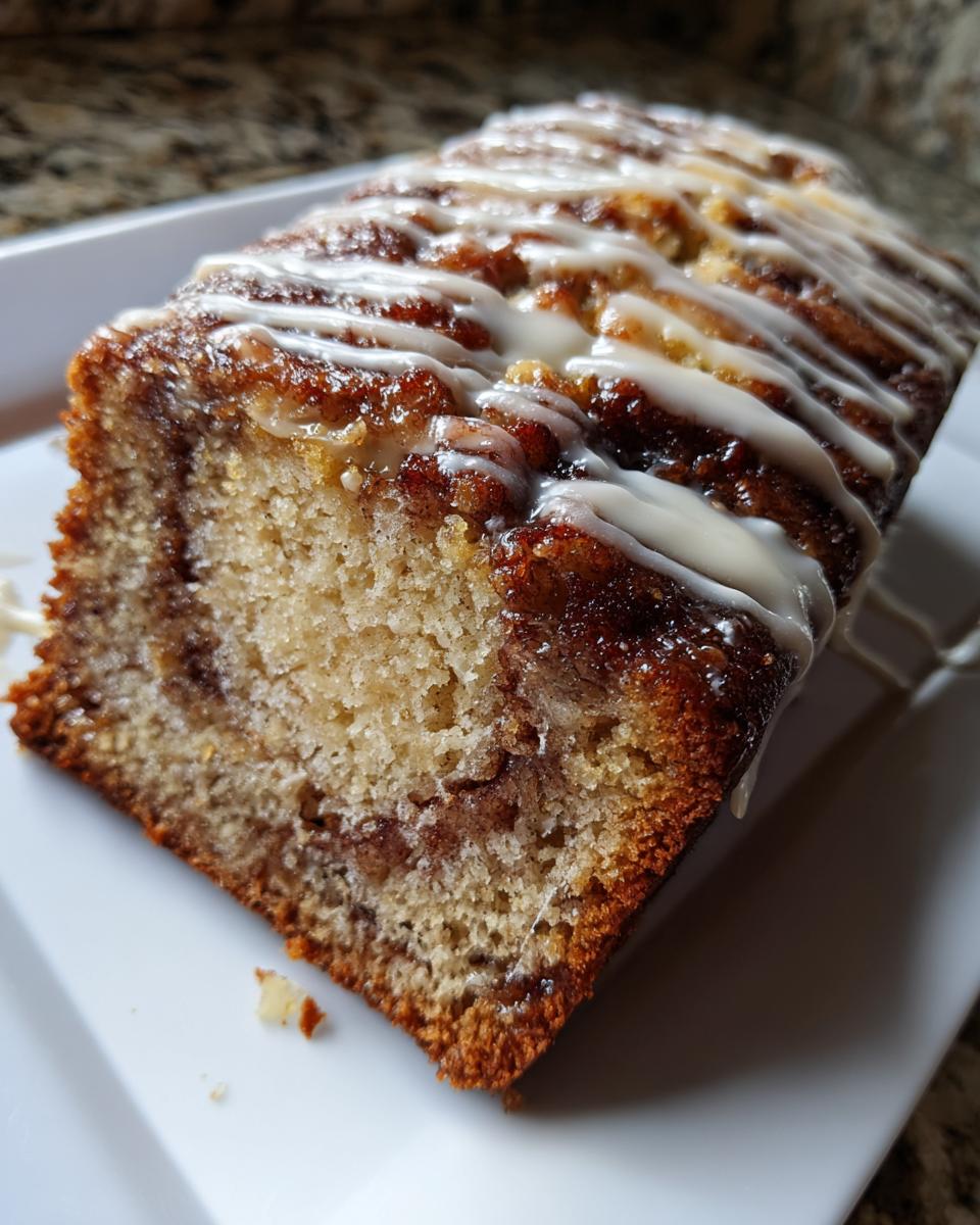 A moist slice of cinnamon roll banana bread featuring a visible cinnamon swirl and topped with a sweet white icing drizzle.