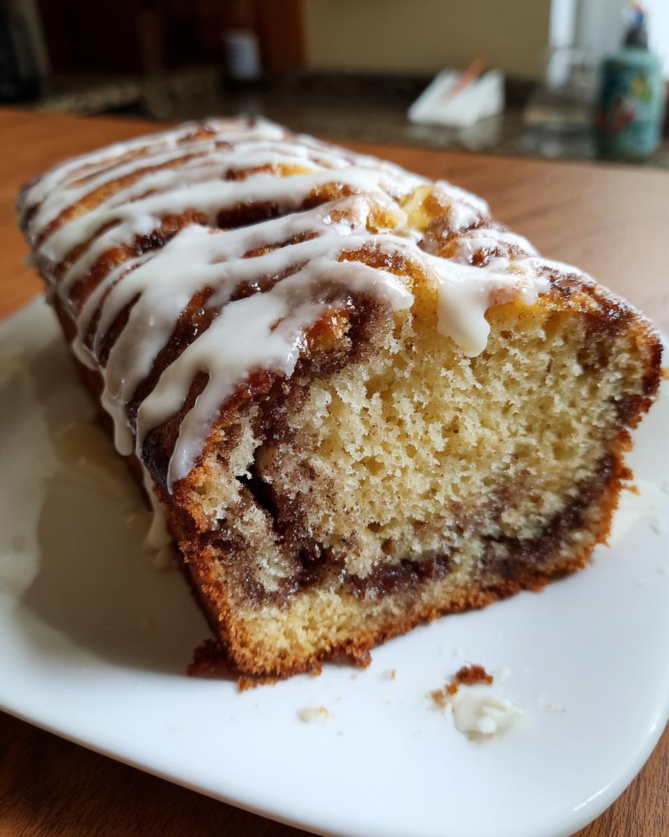 A close-up of a slice of cinnamon roll banana bread showing the swirl and topped with white icing.