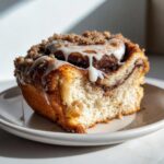 Close-up of a moist slice of cinnamon roll coffee cake topped with white icing and brown sugar streusel.